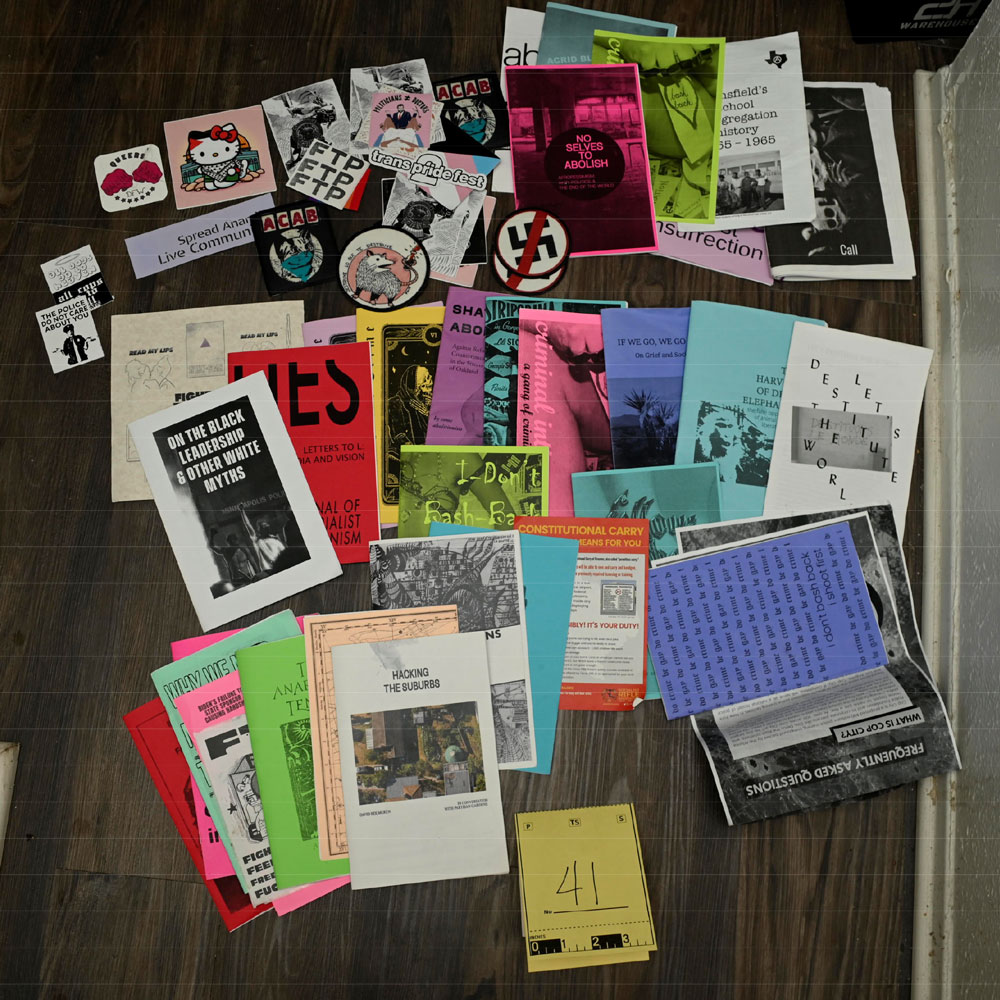 A bunch of zines, stickers, and patches spread out like contraband. There's a yellow evidence number visible: 41.